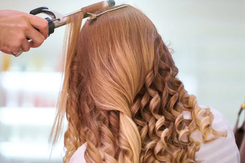 Séance de coiffure et maquillage le matin du mariage — plusieurs femmes en préparation dans une chambre lumineuse, robes accrochées au fond