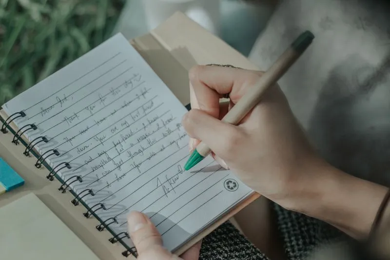 Main écrivant au stylo une courte lettre de remerciement dans un carnet à spirale