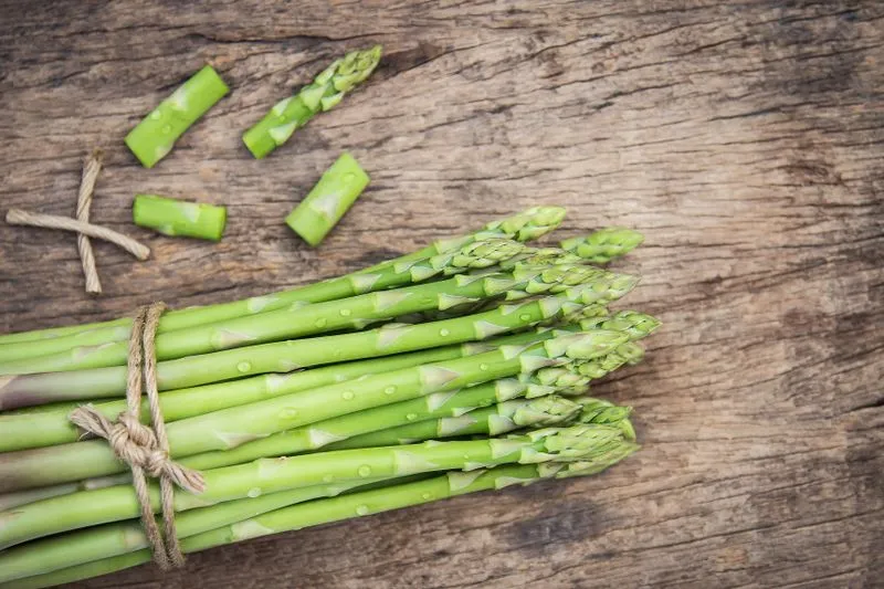 Botte d'asperges vertes ficelée, avec quelques tronçons coupés, sur une planche en bois