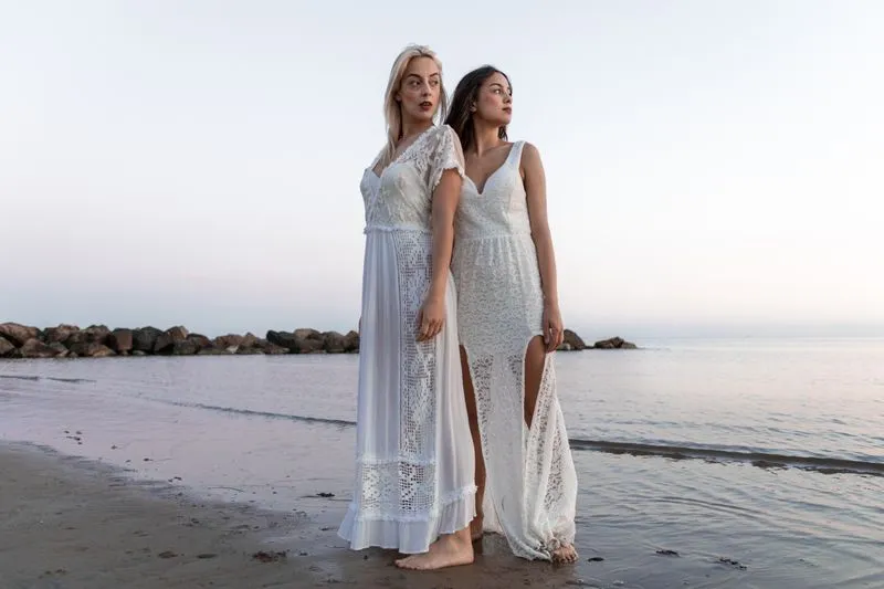 Deux femmes pieds nus au bord de la mer, en robes longues blanches à empiècements de crochet et de dentelle