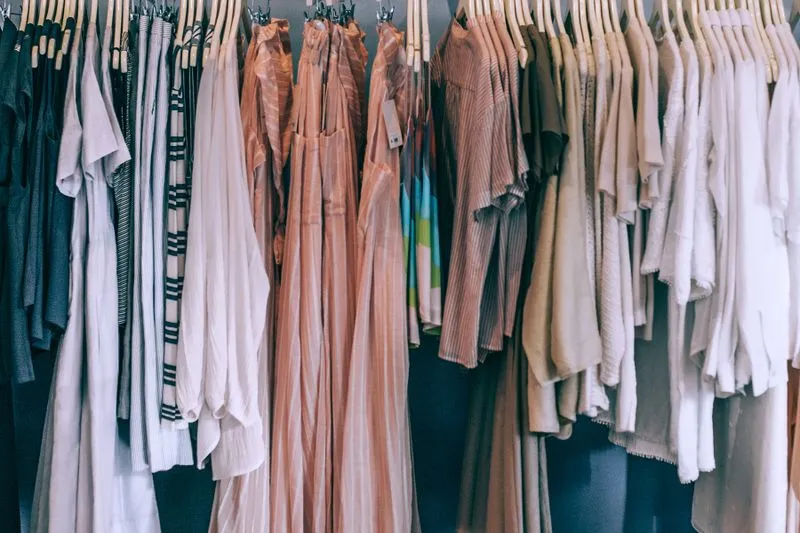 Vêtements d'été fluides aux tons clairs, dont des robes plissées rose terracotta, sur cintres en bois