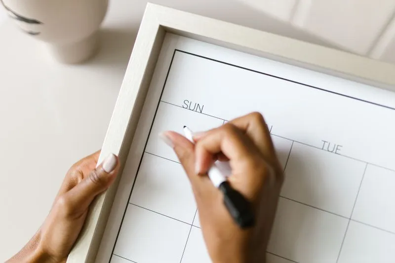 Mains d'une femme notant une date au feutre sur un calendrier hebdomadaire encore vierge