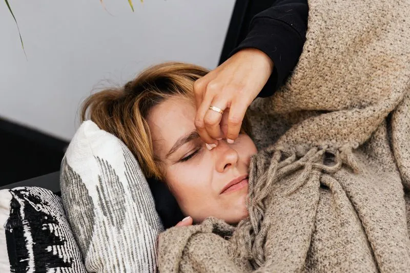 Jeune femme allongée sous un plaid en laine, les yeux fermés, le visage crispé par la douleur
