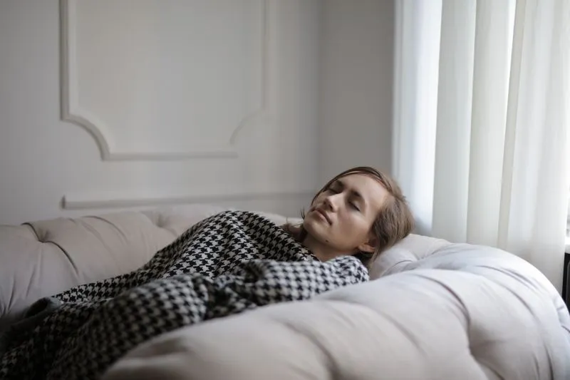 Femme allongée sur un canapé sous un plaid pied-de-poule, les yeux fermés, épuisée
