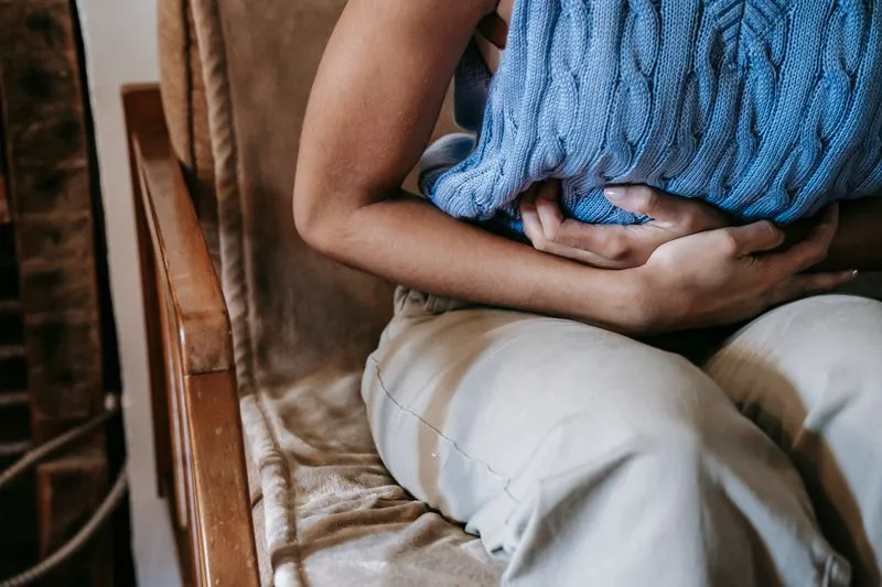 Femme assise dans un fauteuil en bois, les deux mains serrant un coussin en maille bleue contre son ventre