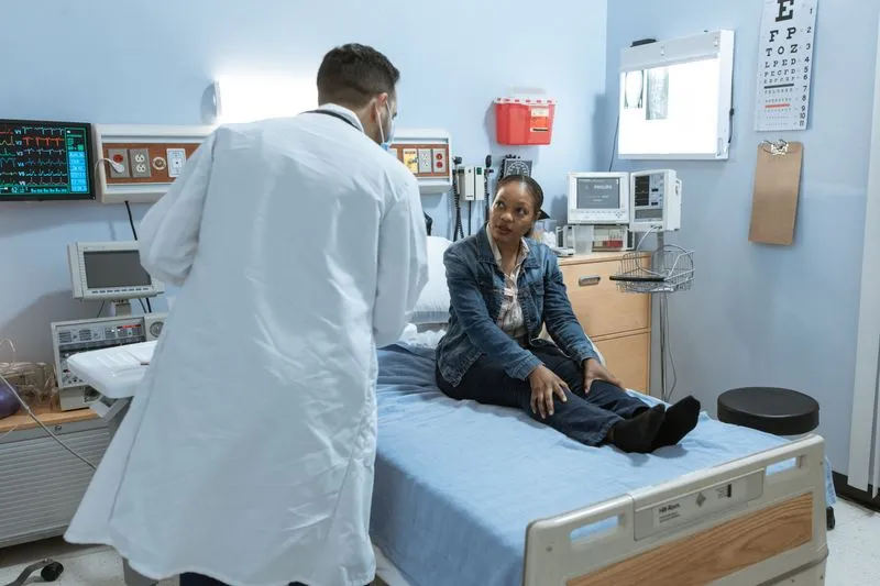 Femme assise sur une table d'examen, en consultation avec un médecin