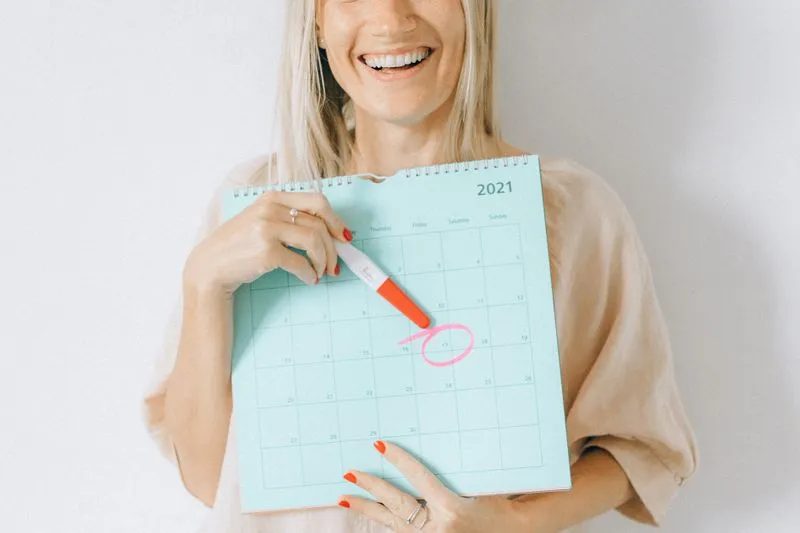 Femme souriante tenant un calendrier et un test, une date entourée