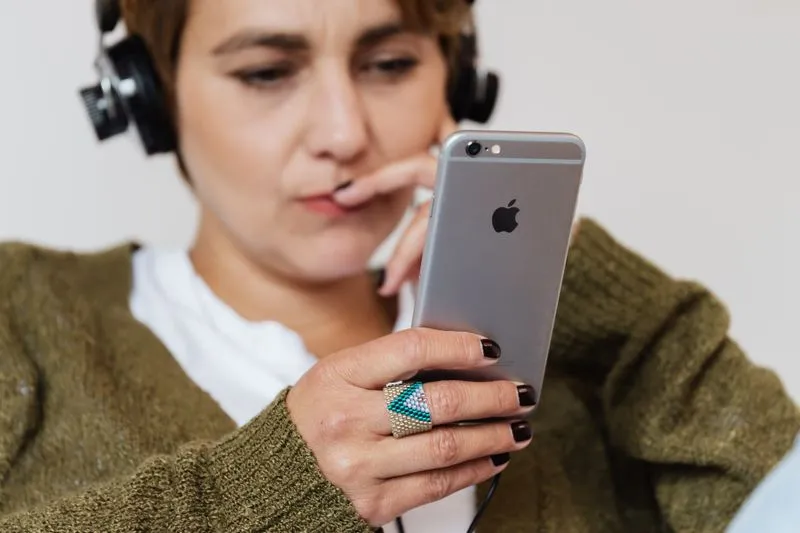 Femme pensive, casque filaire sur les oreilles, les yeux sur son téléphone