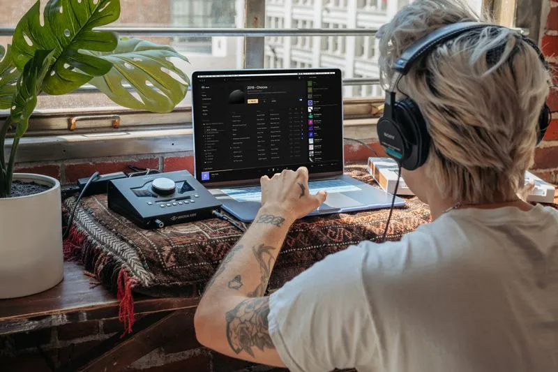 Personne de dos, casque audio sur les oreilles, consultant une liste de morceaux sur son ordinateur portable