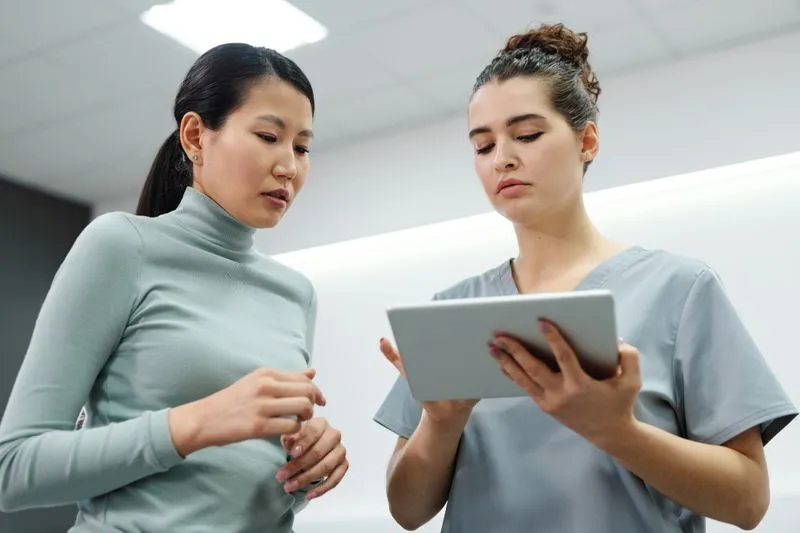 Soignante en tenue médicale qui montre l'écran d'une tablette à une patiente