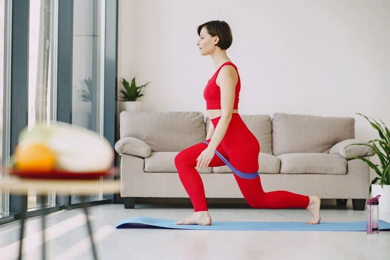 Femme en tenue de sport qui fait une fente avec un élastique sur un tapis, dans son salon