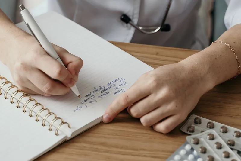 Médecin en blouse blanche prenant des notes à son bureau, à côté de plaquettes de médicaments