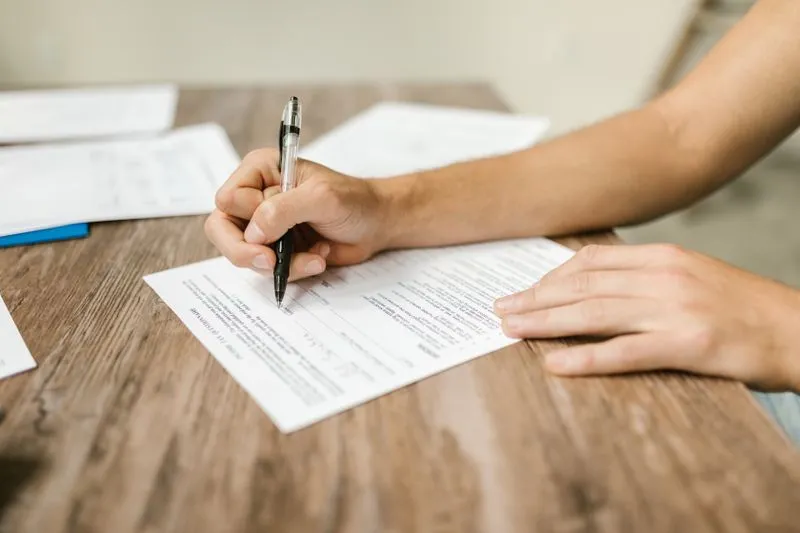 Mains qui remplissent au stylo un questionnaire imprimé, posé sur une table en bois