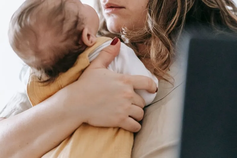 Jeune mère serrant contre elle son nouveau-né en body blanc et barboteuse jaune