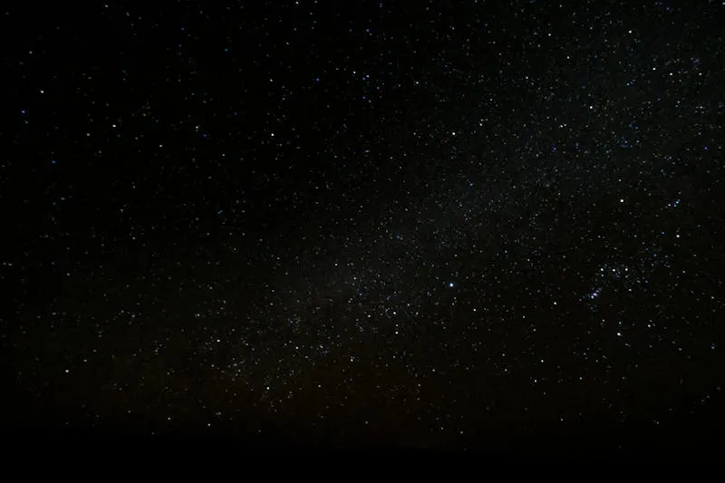 Ciel nocturne constellé d'étoiles au-dessus d'un horizon sombre, avec la traînée pâle de la Voie lactée