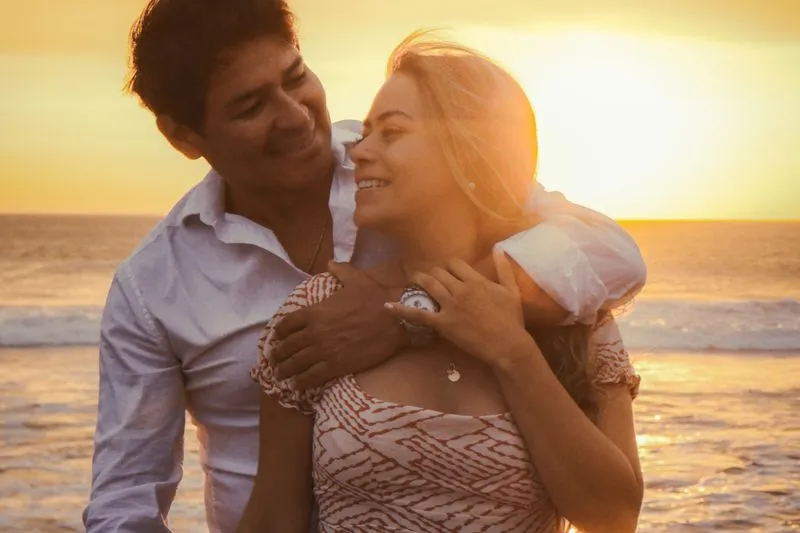 Couple souriant enlacé sur une plage au coucher du soleil, lumière dorée