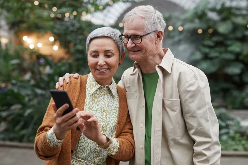 Couple souriant consultant ensemble l'écran d'un smartphone sous une verrière