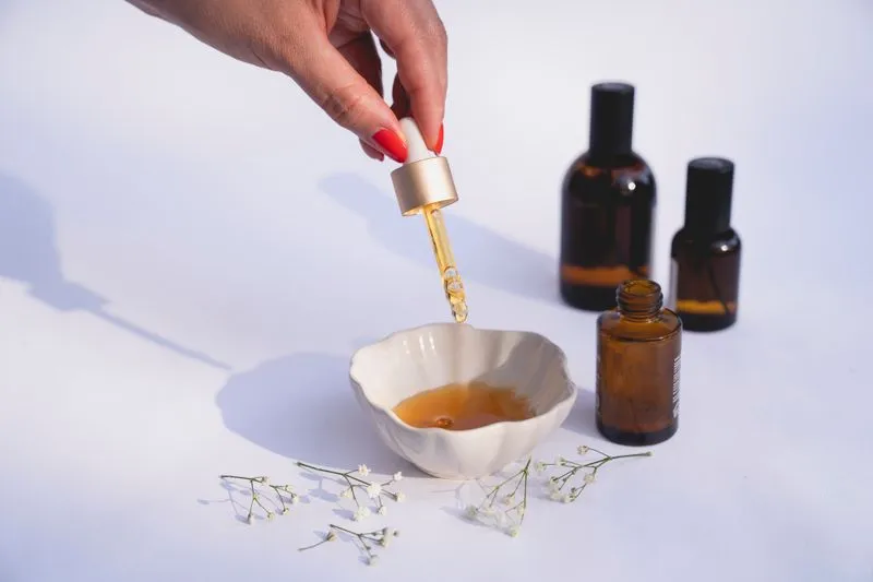 Main qui tient une pipette de sérum doré au-dessus d'une coupelle, flacons ambrés en arrière-plan
