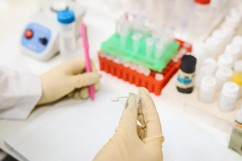 Mains gantées tenant un petit tube dans un laboratoire, portoirs d'éprouvettes en arrière-plan
