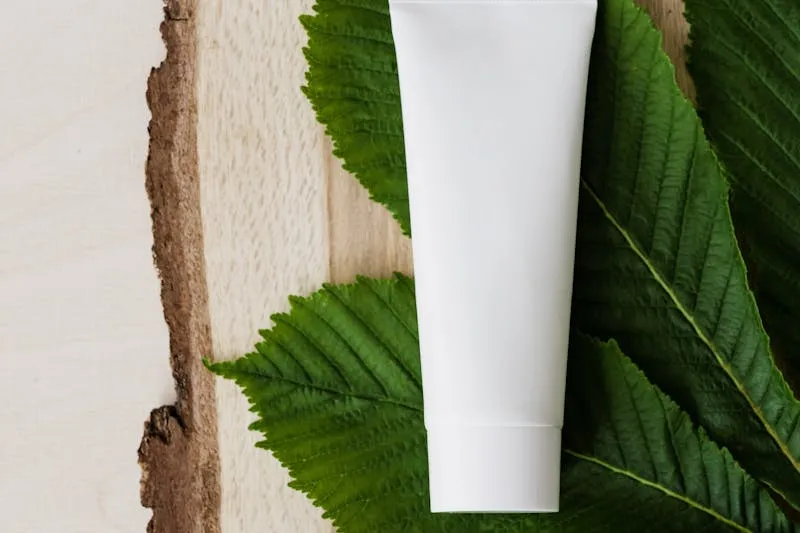 Tube de crème blanc sans marque posé sur de grandes feuilles vertes et une tranche de bois