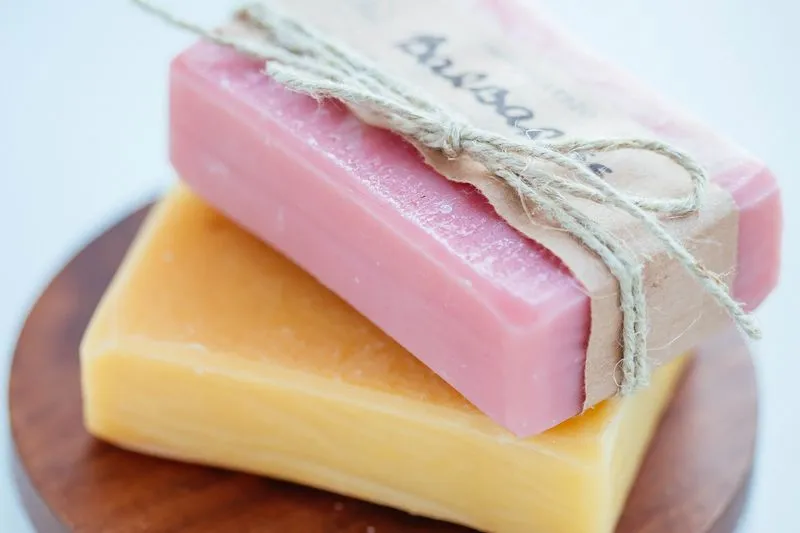 Deux savons artisanaux, rose et jaune, empilés et noués avec de la ficelle, sur un présentoir en bois