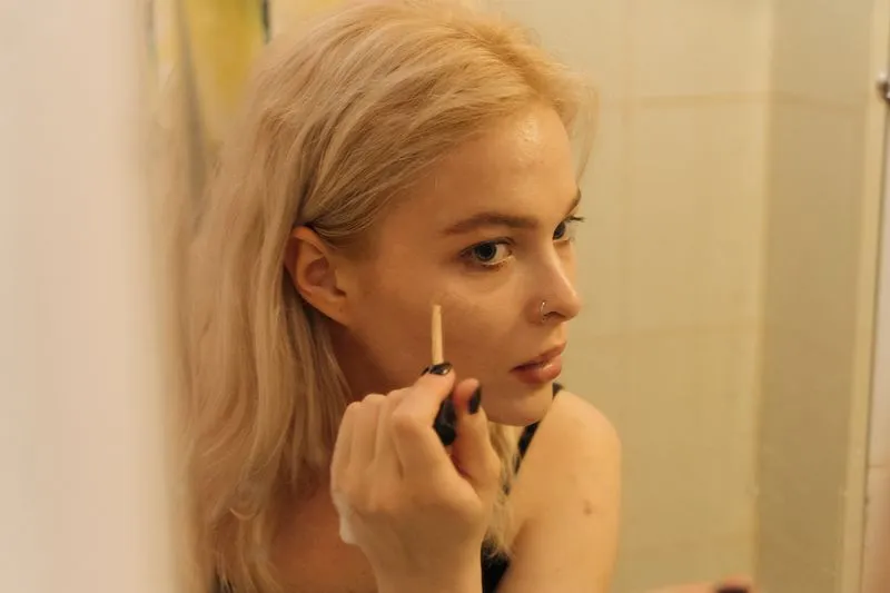 Application minutieuse de maquillage devant un miroir de salle de bain, geste du quotidien