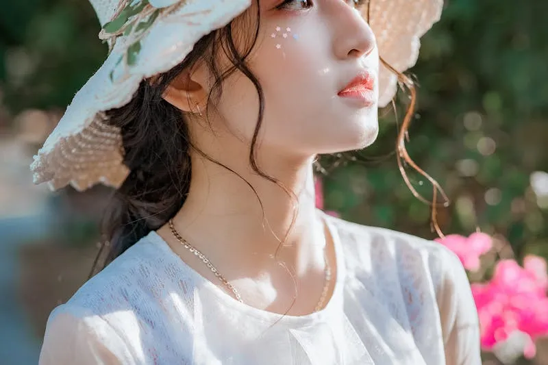 Jeune femme de profil sous un chapeau de paille, peau lumineuse en plein soleil