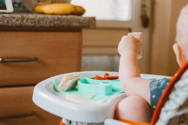 Bébé en DME qui attrape un morceau de pain, des fraises coupées sur son plateau