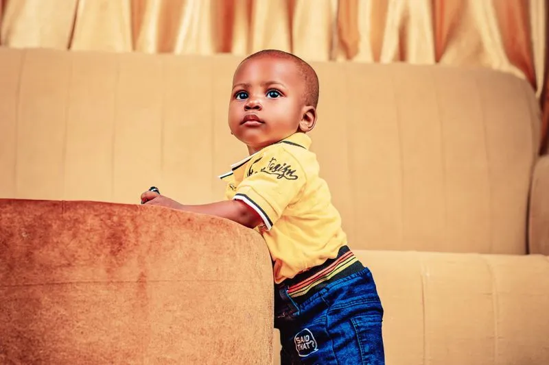 Jeune enfant debout qui se tient à l'accoudoir d'un canapé, le regard levé