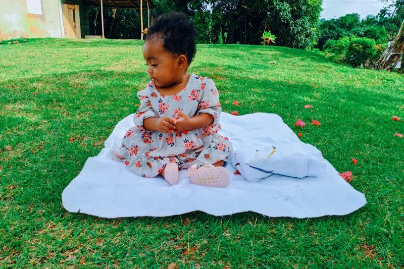 Petite fille assise seule sur une couverture posée dans l'herbe, les mains jointes