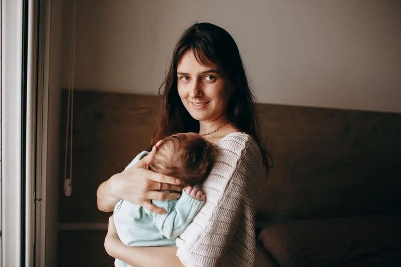 Mère qui tient son nouveau-né blotti contre sa poitrine, près d'une fenêtre