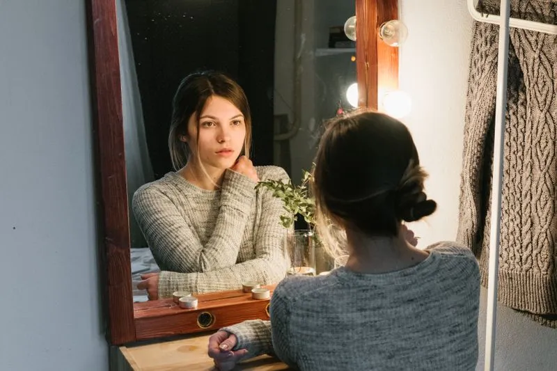 Jeune femme pensive qui observe son reflet dans un miroir, le menton dans la main