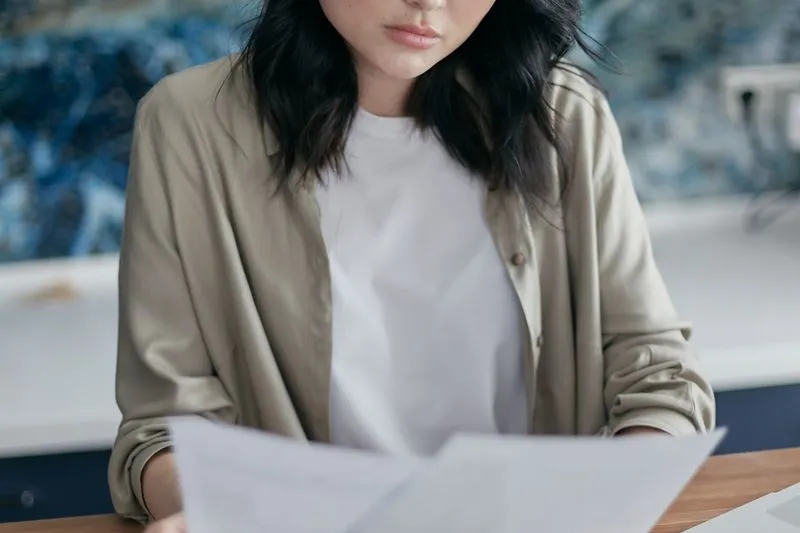 Jeune femme attablée qui lit attentivement des feuilles imprimées