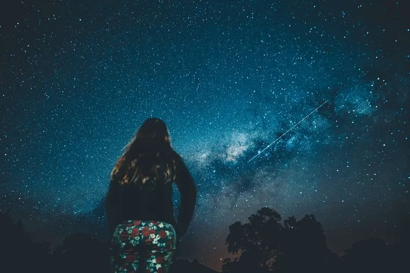 Femme de dos contemplant la Voie lactée dans un ciel nocturne constellé d'étoiles
