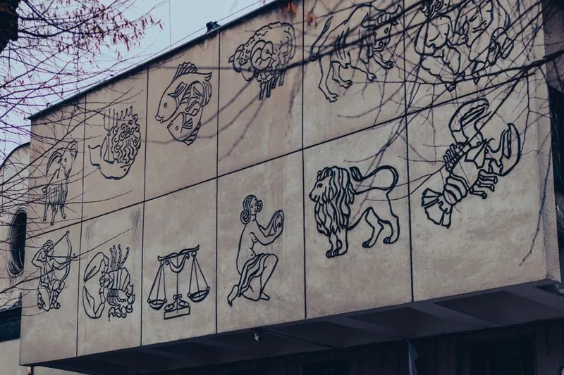 Les douze signes du zodiaque gravés en relief sur la façade d'un immeuble, vus derrière des branches nues