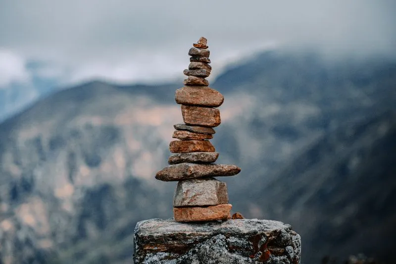 Cairn de pierres empilées en équilibre sur un rocher, devant des montagnes dans la brume
