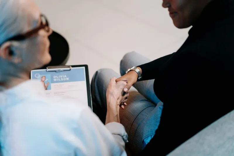 Poignée de main lors d'un entretien entre une femme aux cheveux gris tenant un CV sur un porte-bloc et une femme en pull noir