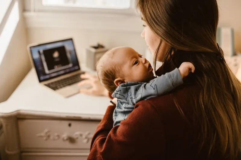 Mère travaillant sur son ordinateur portable tout en portant son bébé contre elle