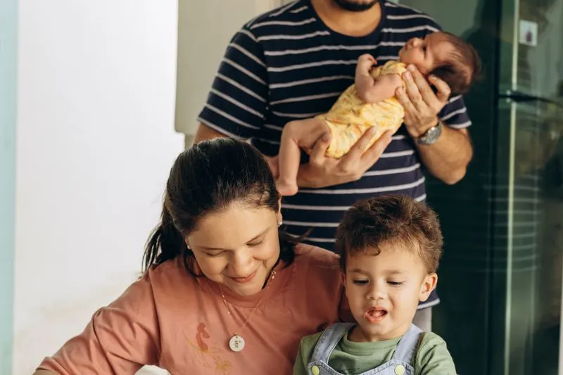 Père portant son nouveau-né, mère souriante avec leur fils aîné à ses côtés
