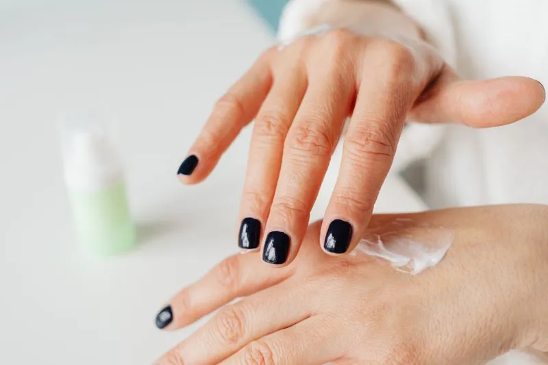 Mains aux ongles vernis bleu nuit qui font pénétrer une crème sur le dos de la main