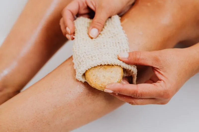 Mains frottant une jambe mouillée avec un gant en sisal et un savon