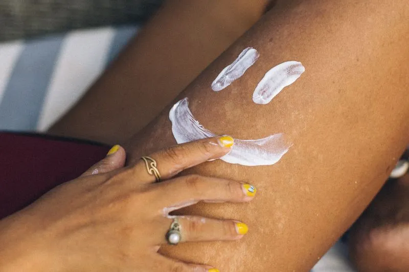 Main aux ongles vernis de jaune étalant de la crème blanche sur une jambe