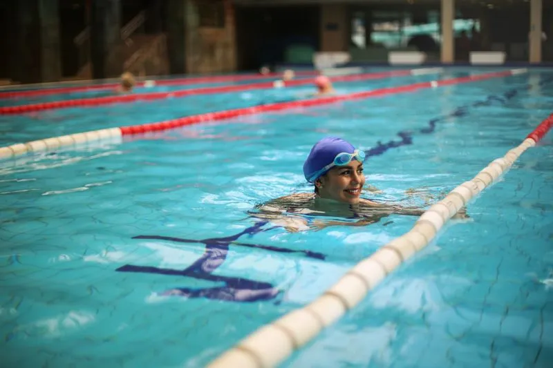 Nageuse souriante en bonnet bleu et lunettes dans le couloir d'une piscine couverte