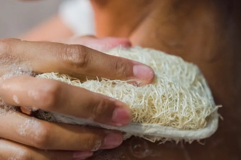 Mains savonneuses qui frottent une éponge loofah sur la peau