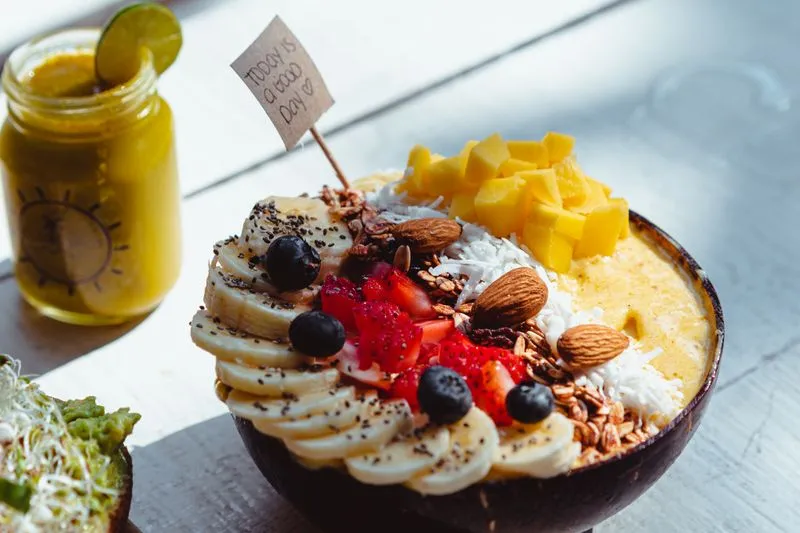 Bol de smoothie coloré à la mangue, à la banane et aux fruits rouges, garni d'amandes et de noix de coco