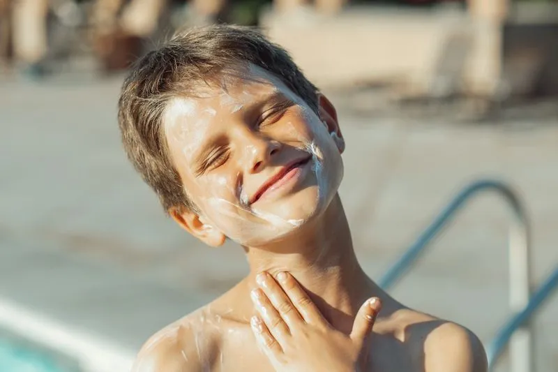 Garçon souriant avec une épaisse couche de crème solaire sur le visage et le cou, au bord d'une piscine
