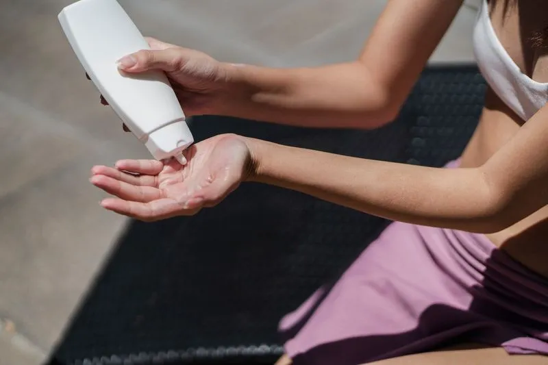 Femme en maillot de bain qui verse une lotion blanche dans sa paume, assise au soleil