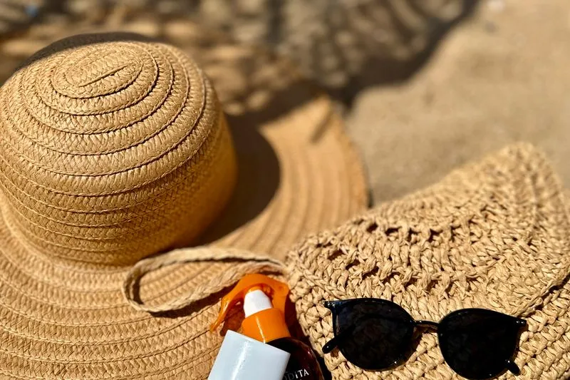 Chapeau de paille, lunettes de soleil et flacon de crème solaire posés sur le sable