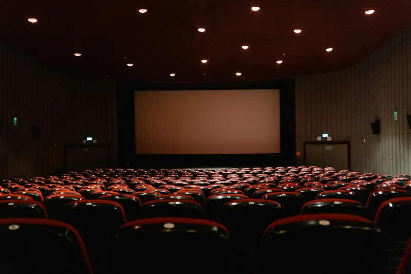 Salle de cinéma vide aux rangées de fauteuils rouges, face à un grand écran blanc