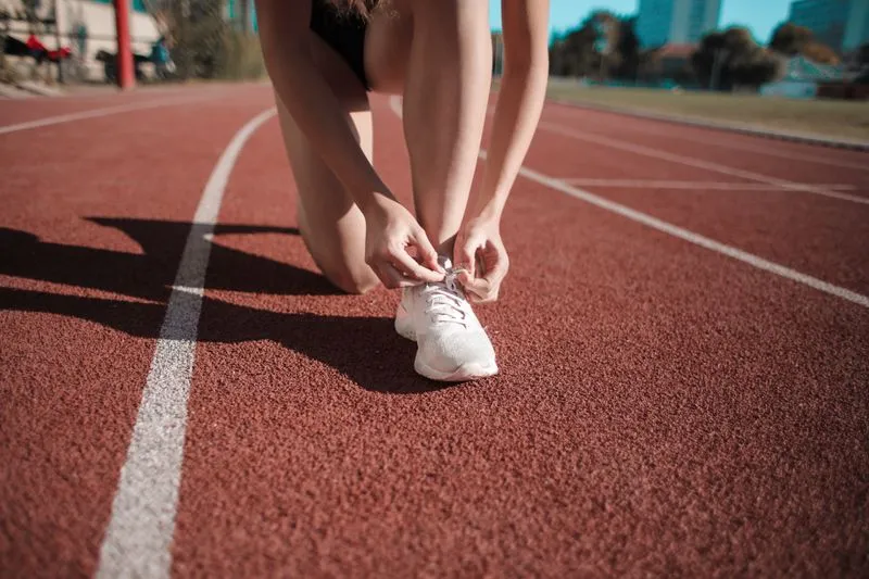 Femme agenouillée sur une piste d'athlétisme qui lace ses chaussures de sport blanches